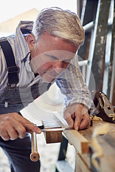 Mature Male Carpenter In Garage Workshop Marking Wood With Pencil And Steel Ruler