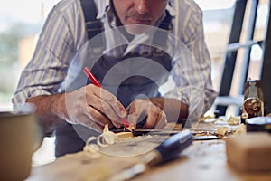 Mature Male Carpenter In Garage Workshop Marking Wood With Pencil And Steel Ruler