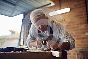 Mature Male Carpenter In Garage Workshop Planing Piece Of Wood