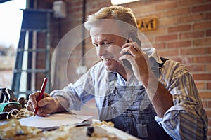 Mature Male Carpenter In Garage Workshop Working On Design And Talking On Mobile Phone