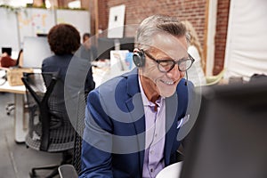 Mature Male Customer Services Agent Working At Desk In Call Center