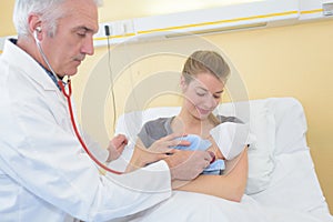 Mature male doctor examining baby girl with mother watching