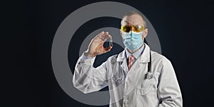 Mature male doctor hold a vaccine in hand in medical protective mask and goggles