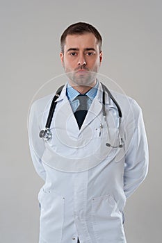 Mature male doctor with serious face standing on grey background