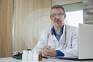Mature Male Doctor Sitting at Desk in Doctor`s Room