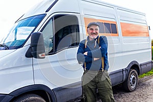 Mature male driver standing in front on his van and looking at camera