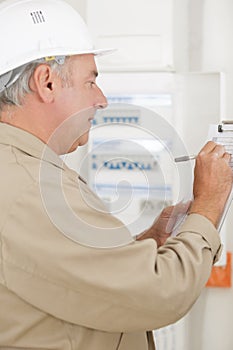 mature male electrician making notes on clipboard