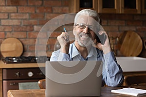 Mature male expert speak by phone distracted from laptop screen