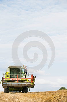 Mature male farmer standing on harvester in field