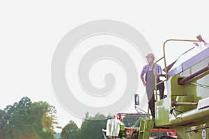 Mature male farmer standing on harvester in field