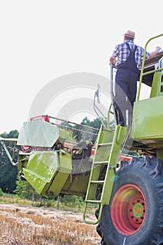 Mature male farmer standing on harvester in field