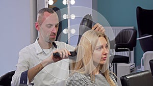 Mature male hairdresser blow drying hair of a female client at the salon