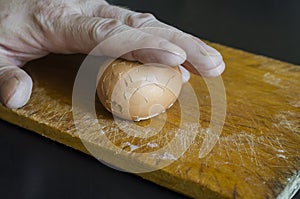 A mature male hand holds a boiled chicken egg in its shell against the chopping board