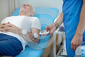 Mature male patient lying on couch, having his muscles stimulated