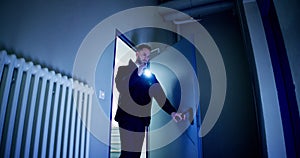 Mature Male Security Guard With Flashlight Standing In Corridor