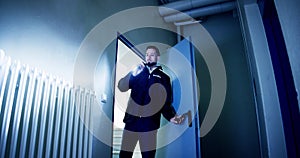 Mature Male Security Guard With Flashlight Standing In Corridor