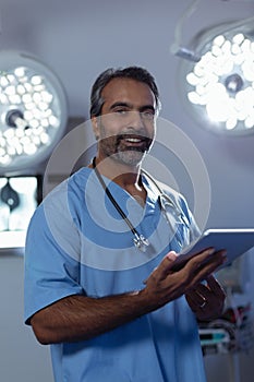 Mature male surgeon looking at camera while using digital tablet in operation room at hospital