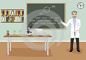 Mature male teacher giving lecture in chemistry class next to blackboard