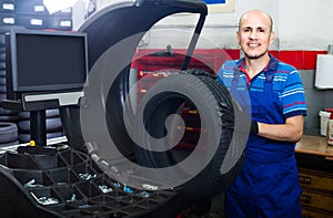 Mature male technician holding car wheel ready to work with balancing machinery at workshop