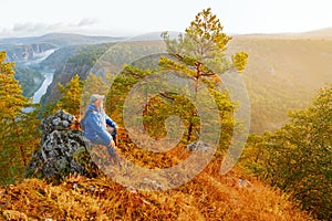 A mature male tourist sits on top of a mountain and admires the picturesque Ural view.