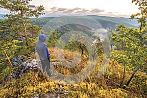A mature male tourist stands on top of a mountain and admires the picturesque morning Ural view.