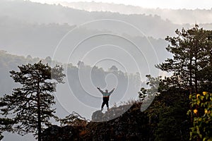 A mature male tourist stands on top of a mountain and admires the picturesque morning Ural view.