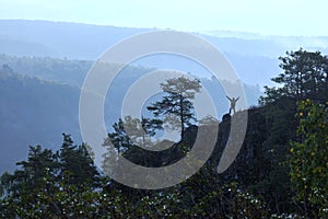 A mature male tourist stands on top of a mountain and admires the picturesque morning Ural view.