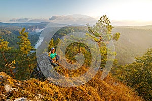 A mature male tourist stands on top of a mountain and admires the picturesque morning Ural view.