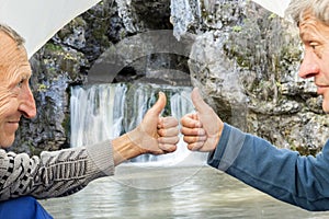 mature male tourists are sitting in a tent and showing their thumb perfectly and admiring beautifully atysh waterfall