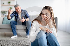 Mature man abusing his depressed wife, shouting, humiliating and threatening her, middle aged woman crying at home