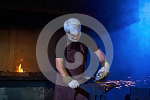 Mature man in apron and gloves processing steel at forge