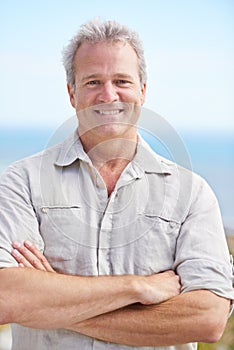 Mature, man and arms crossed in portrait on holiday at beach to travel on adventure or vacation. Smile, outdoor and