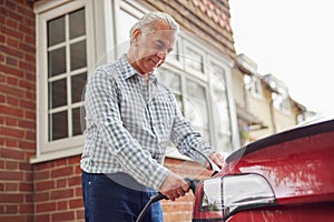 Mature Man Attaching Charging Cable To Environmentally Friendly Zero Emission Electric Car At Home