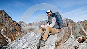 Mature man with backpack hiking in mountains in autumn, resting.