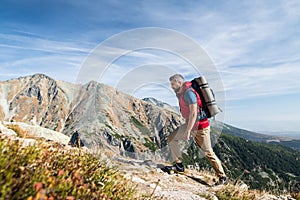 Mature man with backpack hiking in mountains in summer.