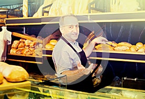 Mature man baker offering fresh baguettes and buns
