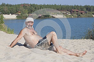 Mature man in a baseball cap and bathing shorts lying on a sandy