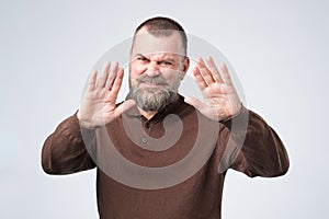 Mature man with beard shows refusal gesture, does not want to speak with you