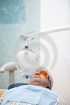 Mature man comfortably seated in dentist`s chair with protective goggles ready to have his teeth whitened