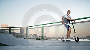 Mature man commuter with electric scooter outdoors in city, going to work.