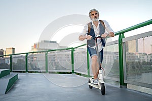 Mature man commuter with electric scooter outdoors in city, going to work.