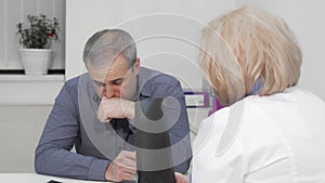 Mature man coughing at medical appointment with his doctor