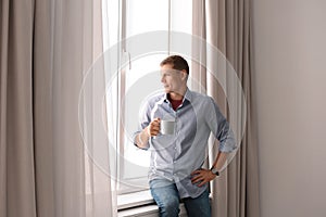 Mature man with cup of hot drink near window