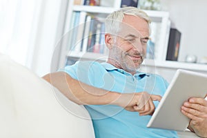 Mature man, digital tablet or relax on sofa in house, home or apartment living room on social media app or internet game