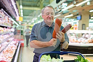 Mature man diligently choosing tasty sausage in supermarket