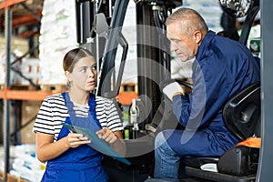 Mature man drive operate automatic fork lift loader and answers young female auditors questions.