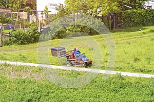 Mature man driving grass cutter in a sunny dGardener driving a riding lawn mower in a gardenay.Worker mowing grass in city park.