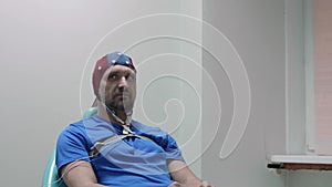 Mature man in EEG cap sits on chair and looks at doctor and smiles.