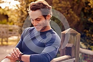 Mature Man Exercising In Countryside Looking At App On Smart Watch