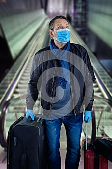 Mature man in a face mask standing in a subway with luggage